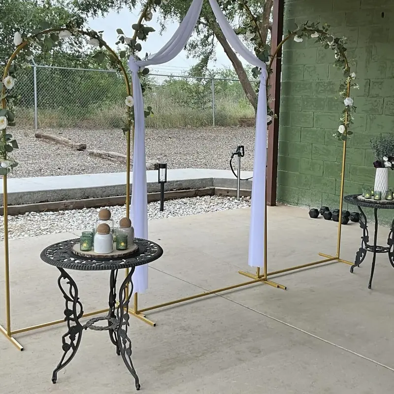 A gold arch with a white drape and greenery on the patio