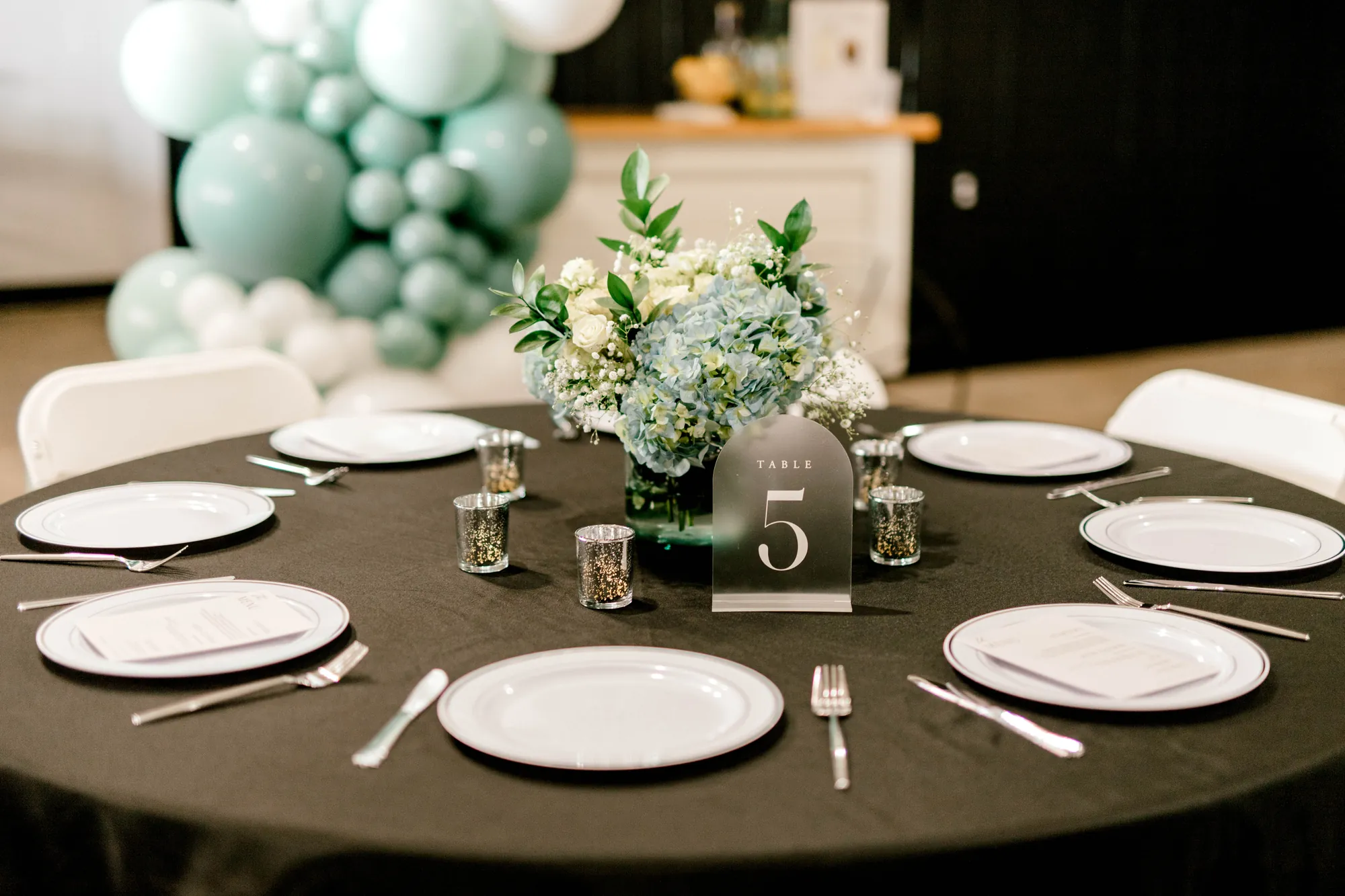 Round table with black linen and a sage balloon garland inside the hall